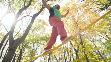 Slackline, spor giyimli sakallı yaşlı bir adam ip üzerinde dengede yürüyor. 50 'li yaşlardaki spor aktiviteleri konsepti
