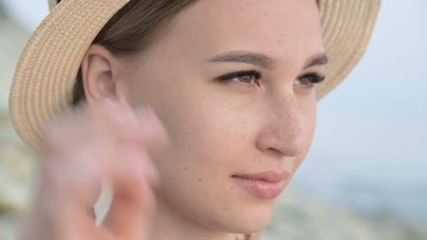 Big close-up face Portrait of an attractive caucasian young woman in a straw hat with pigtails straightens the hat with her hand looks away — Stock Video