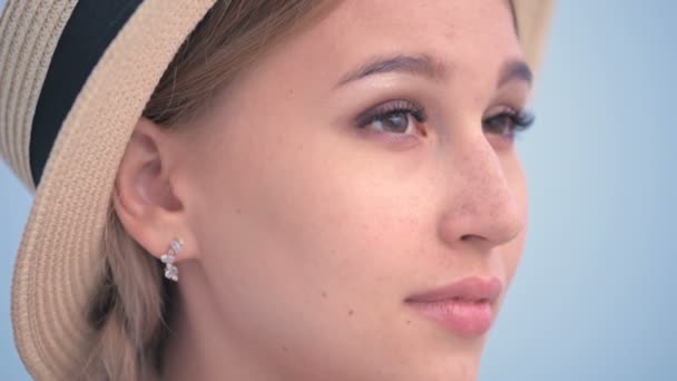 Big close-up face Portrait of an attractive caucasian young woman in a straw hat with pigtails straightens the hat with her hand looks away — Stock Video