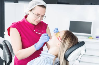 Dişçi ofisinde. Gözlüklü bir kadın diş hekimi genç bir kız hastanın çenebir döküm yapmaya hazırlanıyor. Bakım temiz ağız