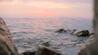 Yakın çekim yavaş çekim düşük açı küçük deniz dalgaları kayalık bir plajda haddeleme. Sahil. Çakıl taşlı kayalık plajda akşam gün batımı