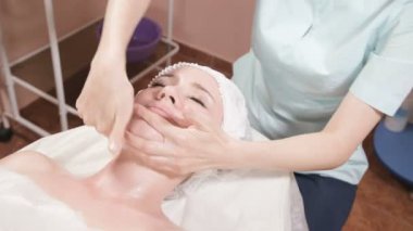 Girl beautician in a mask and gloves makes a salubrious facial massage to an attractive woman. New generation cosmetology massage