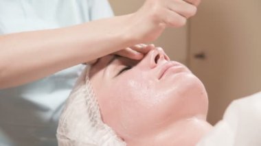Girl beautician in a mask and gloves makes a salubrious facial massage to an attractive woman. New generation cosmetology massage