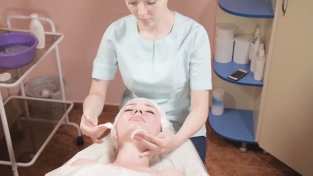 Chica esteticista en una máscara y guantes hace un masaje facial saludable a una mujer atractiva. Masaje cosmetológico de nueva generación — Vídeos de Stock