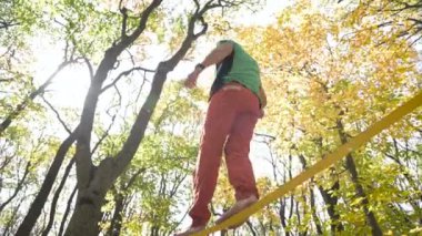 Slackline, spor giyimli sakallı yaşlı bir adam ip üzerinde dengede yürüyor. 50 'li yaşlardaki spor aktiviteleri konsepti