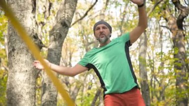 Spor kıyafetleri içinde sakallı, gevşek bir adam ip üzerinde dengede yürüyor. 50 yaşındaki spor aktiviteleri konsepti