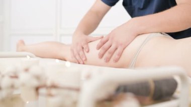 Yakın çekim bir erkek fizyoterapist pamuk bir delikanlı yanında profesyonel bir spa salonunda genç bir kadının kalça ve kalça ısınmak için hafif bir masaj yapıyor. 4k masaj vücut bakım konsepti
