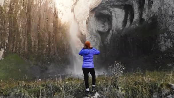 Een meisje is een professionele landschapsfotograaf die op een steen bij de rivier staat en een grote epische waterval fotografeert. Luchtfoto 's. Noord-Kaukasus — Stockvideo