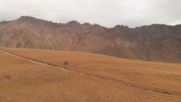 一对头戴大背包、戴着太阳镜、头戴大背包的男女旅行者沿着高山高原漫步的空中景象 — 图库视频影像