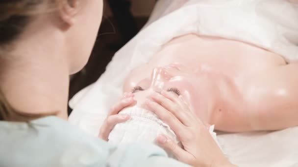 Zbliżenie Spa masaż twarzy. Dziewczyna profesjonalny masażysta robi relaksujący masaż twarzy do atrakcyjnego klienta salonu spa — Wideo stockowe