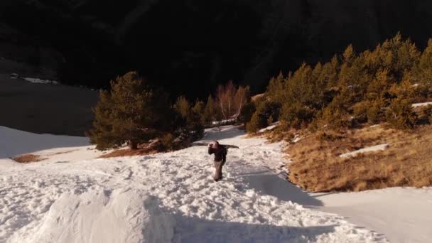 Hava manzaralı sporcu kız sporcu yayan olarak yamacın yamacında omuzlarında bir snowboard ile Kafkasya dağlarındaki bir ev noktasında vurucunun yanına tırmanıyor.. — Stok video