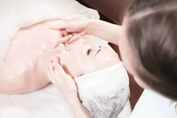 Una masajista profesional le hace un masaje facial a un cliente en un salón de cuidado facial de spa. El concepto de masaje facial y cuidado de la piel —  Fotos de Stock