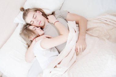 Genç, uzun saçlı bir çift, erkek ve kadın yatakta sarılarak uyur. Genç bir ailede sağlıklı uyku kavramı