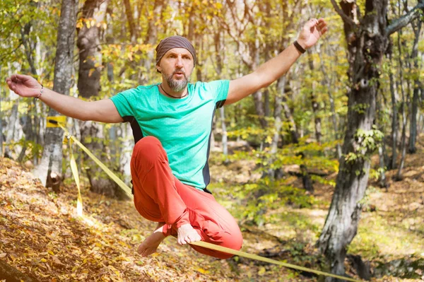 Um homem barbudo envelheceu balanceando em um slackline na floresta de outono em um dia ensolarado. O conceito de lazer desportivo aos quarenta anos — Fotografia de Stock