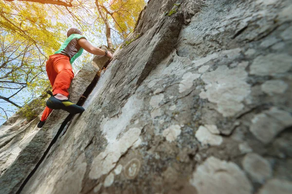 Um homem está treinando em escalada livre em uma pedra de rocha na floresta em um dia ensolarado. O conceito de atividades de lazer de um estilo de vida ativo de pessoas com idade — Fotografia de Stock