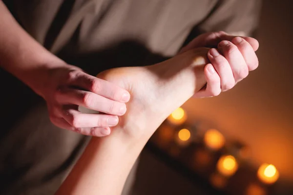 Close-up professional calf muscle massage to a female client by a male physiotherapist in a massage parlor in a dark office against the background of burning candles — Stock Photo, Image