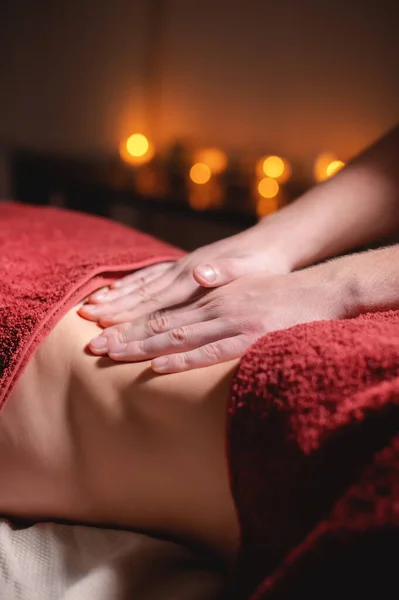 Close-up de massagistas mãos masculinas fazendo massagem abdominal a uma cliente feminina em um escritório escuro contra o fundo de velas acesas . — Fotografia de Stock