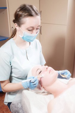 Kozmetik salonundaki profesyonel bir güzellik uzmanı müşterinin yüzüne canlandırıcı bir maske takıyor. Koruyucu maskeli bir güzellik uzmanı. Virüs salgını sırasında kozmetoloji