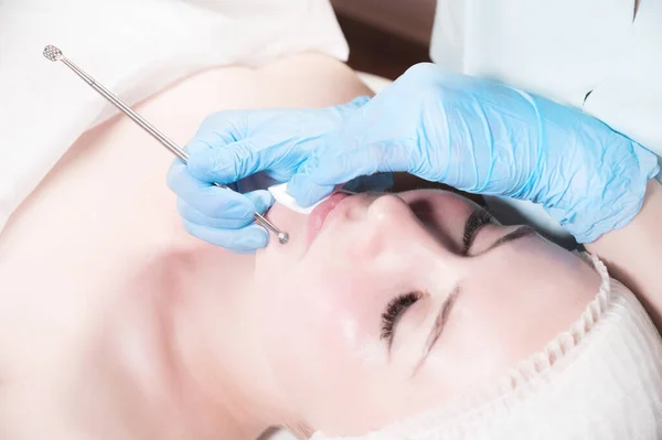 Close-up Mechanical face peel at the beautician. Beautician squeezes acne on the patients forehead with a medical needle. Face next to hands in blue gloves of cosmologist — Stock Photo, Image