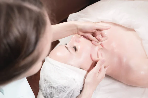 Una masajista profesional le hace un masaje facial a un cliente en un salón de cuidado facial de spa. El concepto de masaje facial y cuidado de la piel — Foto de Stock