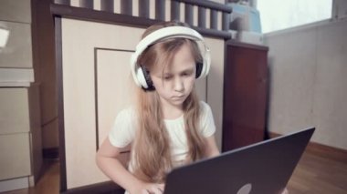 Yedi yaşında, elinde dizüstü bilgisayarla beyaz kulaklıklı akıllı bir kız odasında yere bastırıyor. İnternet ve bilişim teknolojisindeki genç nesil.