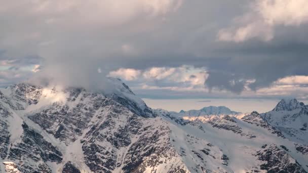 Timelapse desde una altura de 4000 metros de altura cubierto de nieve rocas con glaciares y montañas de la cresta principal del Cáucaso con la puesta del sol por la noche nubes de color naranja y glaciares en las cimas de las montañas . — Vídeo de stock