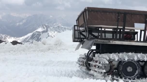 Primer plano de trabajo de orugas anchas de paseos de snowcat en la nieve y rastrillos contra el telón de fondo de las montañas nevadas. concepto de preparación de pistas de nieve para la temporada de esquí y la cosecha de nieve — Vídeo de stock