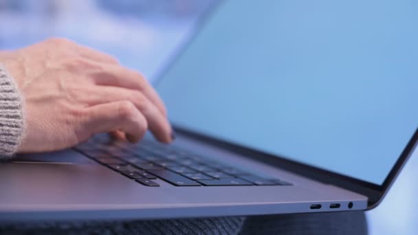 Primer plano manos femeninas escribiendo en un teclado portátil por la noche cuando la hora azul ya ha llegado fuera de la ventana. Profundidad de campo superficial. bosque de invierno en el fondo. Concepto independiente — Vídeo de stock