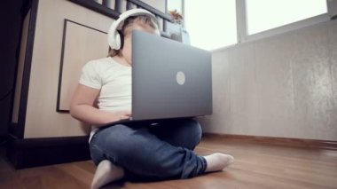 Yedi yaşında, elinde dizüstü bilgisayarla beyaz kulaklıklı akıllı bir kız odasında yere bastırıyor. İnternet ve bilişim teknolojisindeki genç nesil.