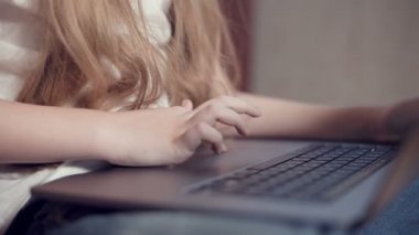 Laptop klavyesinde küçük bir kızın elinin sığ derinliği. Genç nesil aletleri kullanma fikri.