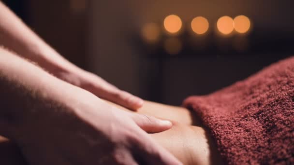 Close-up Jonge mannelijke massage therapeut doet rug massage aan een vrouw met een tatoeage in een massageruimte met schemerige lichten op de achtergrond van kaarsen. Low-key premium massageconcept — Stockvideo