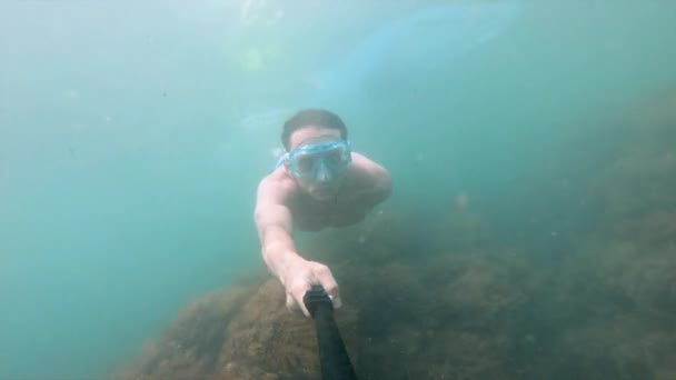 Hombre musculoso con máscara nada bajo el agua, sosteniendo la cámara delante. Primer plano . — Vídeos de Stock