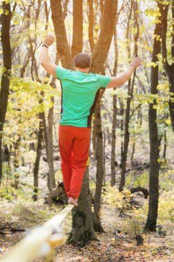 Yaşlanmış sakallı bir adam güneşli bir öğleden sonra sonbahar ormanında ip boyunca yürür. Aktif orta yaşlı insanların eğlence ve yeniden canlandırma konsepti