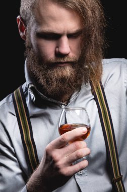 Uzun sakallı ve bıyıklı çekici bir adam duvarda oturmuş elini tutan bir bardaktaki alkollü içeceğin kokusunu kokluyor..