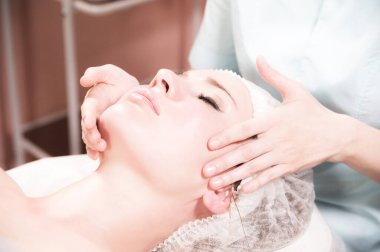 Profesyonel bir kadın masaj terapisti kaplıca salonundaki müşterisine yüz masajı yapıyor. Yüz masajı ve cilt bakımı kavramı