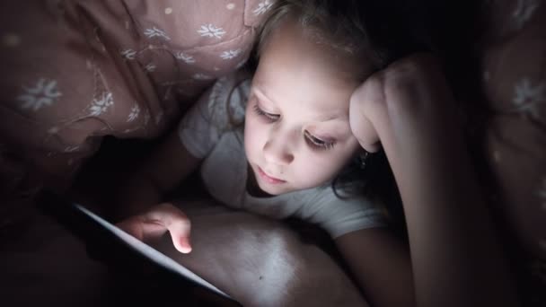 Mladá holčička se schovává pod přikrývkou, aby mohla používat digitální tabletový smartphone pozdě po spánku. Osamělost malých dětí a záchrana na telefonu. — Stock video