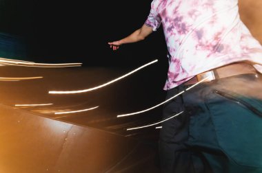 Büyük bir plan, kaykaylı bir sporcunun gece kaykaylı bir parka hızlıca binmesidir. Şehirdeki gösterişli gençlik gece hayatının bir derlemesi. Hareket halindeki kayganlaştırıcının uzun süre maruz kalması