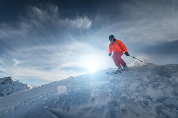 Skifahrer fährt an einem sonnigen Tag bei Sonnenuntergang auf einem schneebedeckten Hang vor der Kulisse der Berge. Das Konzept des Winterskifahrens — Stockfoto