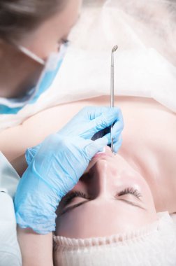 Mekanik yüz, güzellik uzmanına yakın çekim. Güzellik uzmanı, hastanın alnına tıbbi bir iğneyle sivilce sıkıyor. Kozmolojistin mavi eldivenleriyle ellerin yanında.