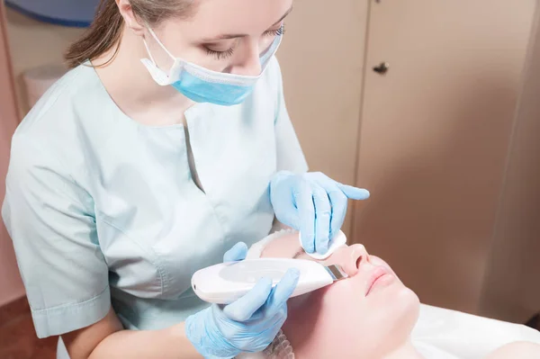 Cosméticos e cuidados faciais. Menina atraente na recepção de um esteticista no salão de beleza faz a limpeza e descascamento do rosto com ultra-som. Pele facial bonita e saudável — Fotografia de Stock