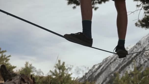 Un joven se tambalea en una línea floja en las montañas del norte del Cáucaso. Primer plano de las piernas de atleta en medio de montañas cubiertas de nieve — Vídeos de Stock