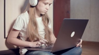 Yedi yaşında, elinde dizüstü bilgisayarla beyaz kulaklıklı akıllı bir kız odasında yere bastırıyor. İnternet ve bilişim teknolojisindeki genç nesil.
