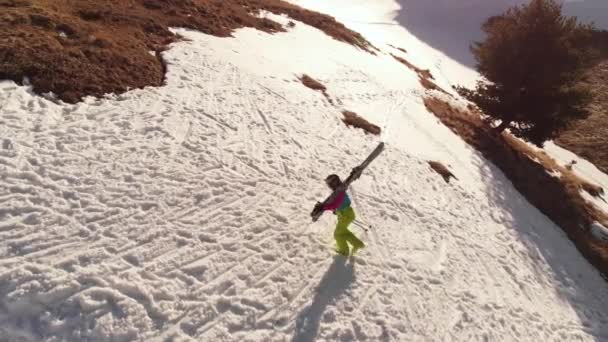 空中ビューの女の子アスリートのスキーヤーは、コーカサス山脈のホームスポットでキッカーの横にある彼の肩の上のスノーボードで斜面に沿って徒歩で登る. — ストック動画