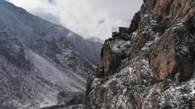 Kameranın yakın açıklığının havadan görüntüsü dağların yükseklerinde bir kaya duvarının yanında ilkbaharın başlarında yeşil çimenler ve dağların yamaçlarında kar.