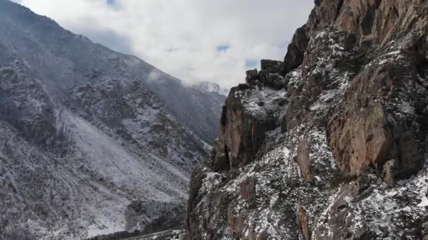 Vista aérea del tramo cercano de la cámara junto a una pared de roca en lo alto de las montañas a principios de primavera hierba verde y nieve en las laderas de las montañas — Vídeo de stock