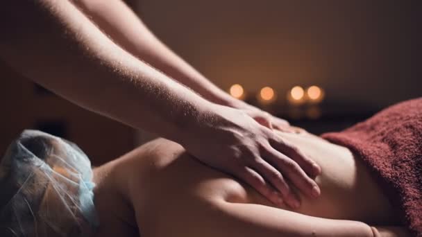 Close-up Young male massage therapist does back massage to a woman with a tattoo in a massage room with dim lights on the background of candles. Low key premium massage concept — ストック動画