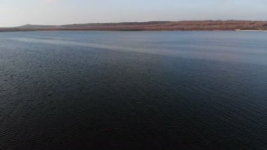 Gün batımından sonraki akşam alçaktan uçan bir dronun pürüzsüz yüzeyi üzerindeki hava görüntüsü. Yerel doğal su kaynağına sahip arka plan videosu