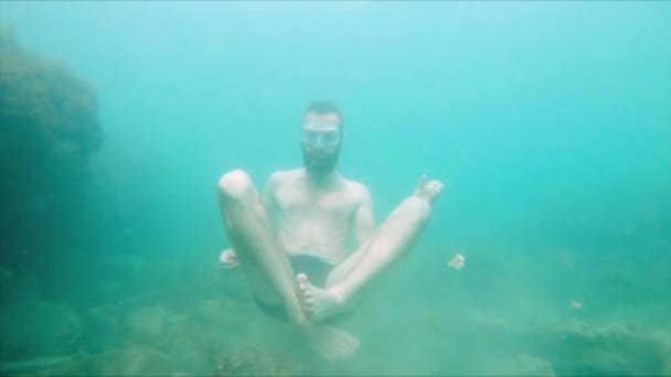 Déplaçant lentement un jeune homme barbu tente de méditer dans une pose de lotus au fond de la mer dans l'eau. Le concept de méditation zen et yoga sous-marin — Video