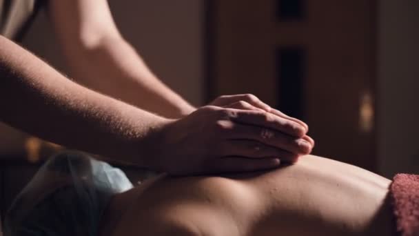 Um jovem massagista do sexo masculino faz uma menina cliente de massagem profissional em uma sala de massagem profissional com velas acesas em um quarto escuro — Vídeo de Stock