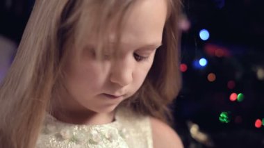 Şenlik ışıkları ve Noel ağacının arkaplanına karşı şenlikli bir elbise giymiş küçük bir kız ne yazık ki bulanıklığın içinde bir yere bakıyor ve odaklanma hareketi yapıyor. Bozuk tatil kavramı